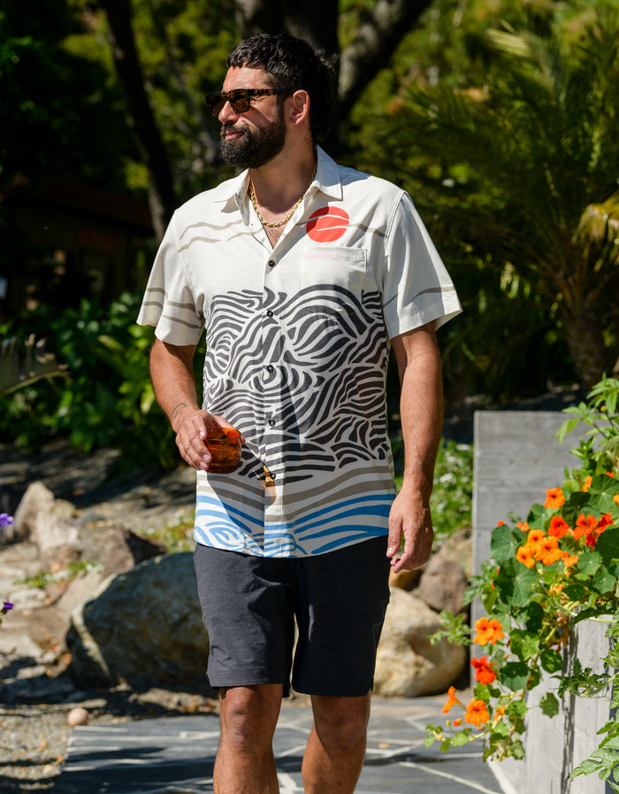 Man walking outdoors wearing Baja Llama Magellan Explorer Shorts in Black Heather, styled with a patterned button-down shirt for a casual, adventurous look.