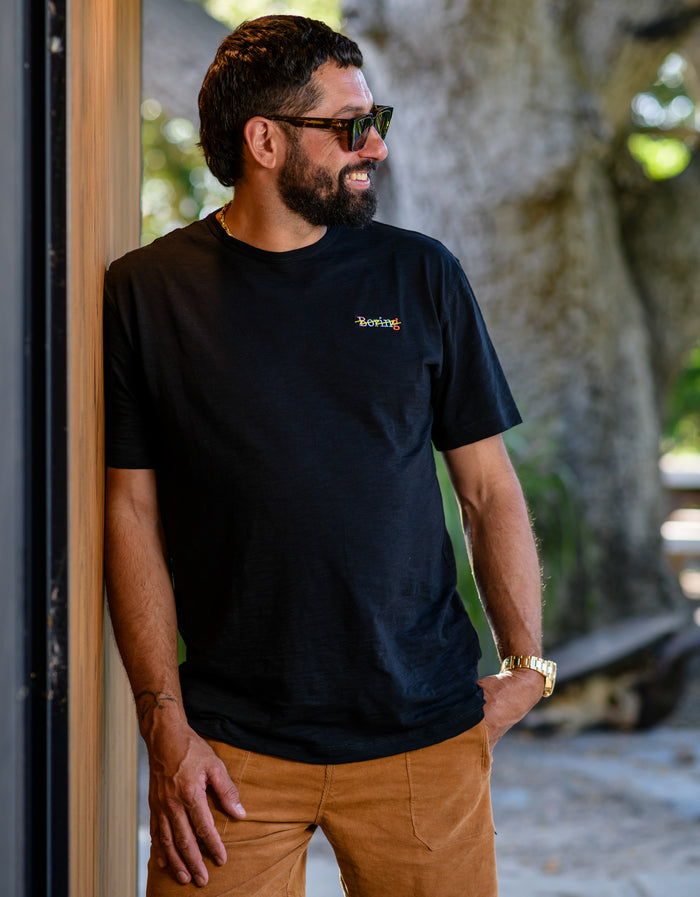 Man wearing Baja Llama black slub pima cotton t-shirt with colorful "Boring" embroidery.