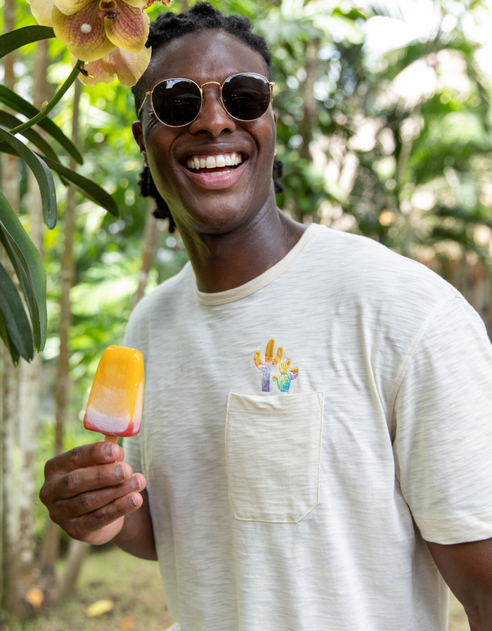 Smiling man wearing a cream Baja Llama Colorful Cactus Slub Pima Pocket Tee while holding a popsicle.