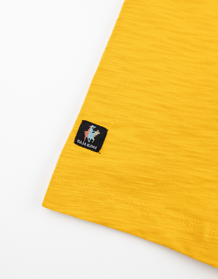 Close-up of the Baja Llama brand tag on the hem of the yellow El Sativo Agave slub pima pocket tee.