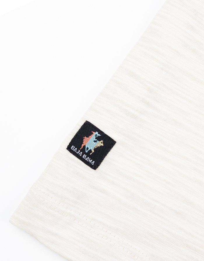 Close-up of the Baja Llama brand tag on the hem of the cream Colorful Cactus Slub Pima Pocket Tee.