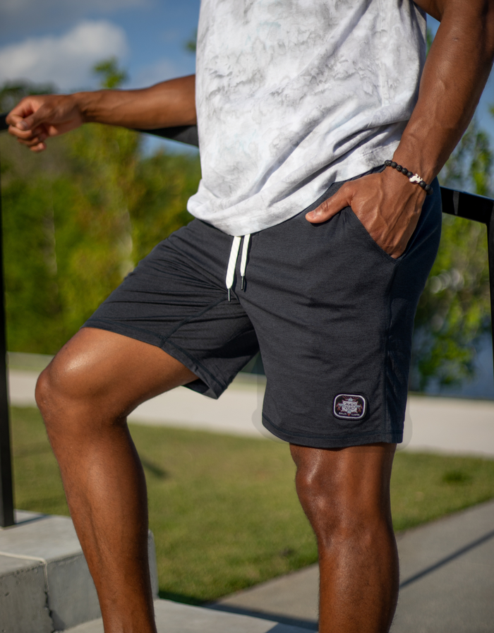 A man modeling black Mach Zero lounge shorts by Baja Llama, featuring a branded patch and drawstring waist in an outdoor setting.