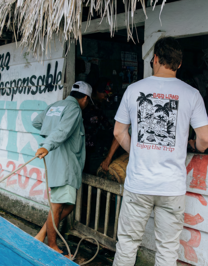 Man wearing a white Baja Llama "Enjoy The Trip" Primo Graphic Tee in a lifestyle setting.