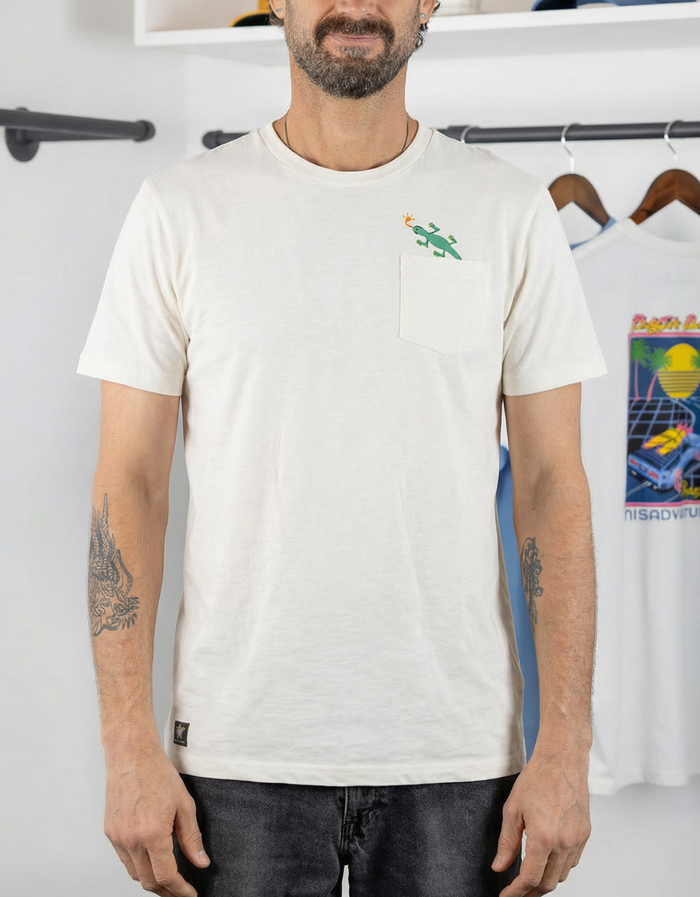 A male model with arm tattoos standing and wearing the Baja Llama Thin Lizzy Pima Slub Pocket Tee, featuring a small embroidered green lizard climbing out of the left chest pocket.