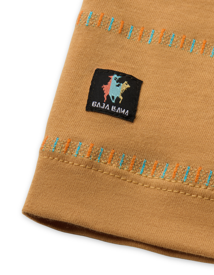 Close-up of a mustard yellow/camel fabric with colorful stitching and a logo label on a white background