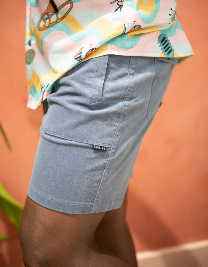 Side lifestyle view of steel blue Arroyo corduroy walkshorts with Boring hem tag and wavy print shirt