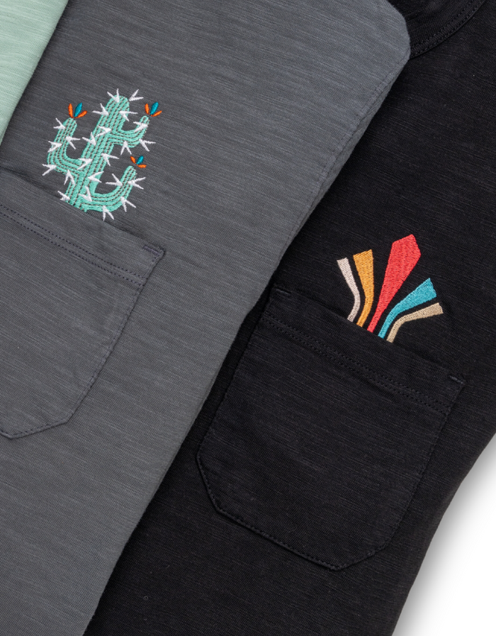 Close-up of Baja Llama Retro League slub pima pocket tee in black with colorful retro chest embroidery.