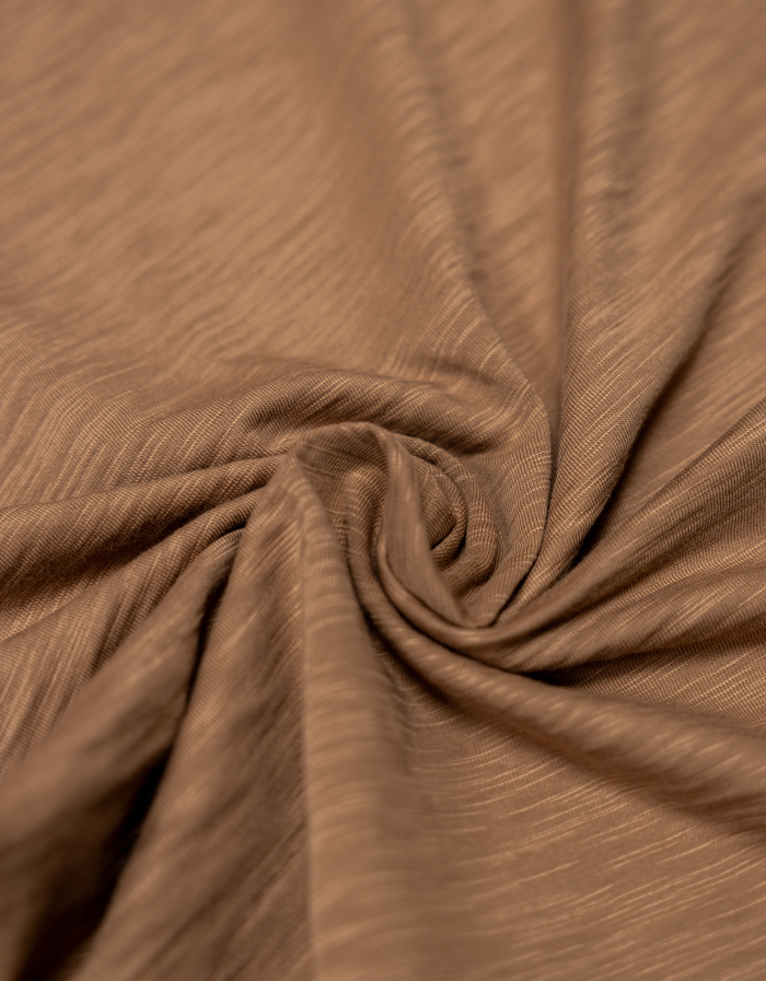 Detailed close-up of a soft, scorched brown slub-knit cotton fabric arranged in a spiral, showing the fine texture and weave.