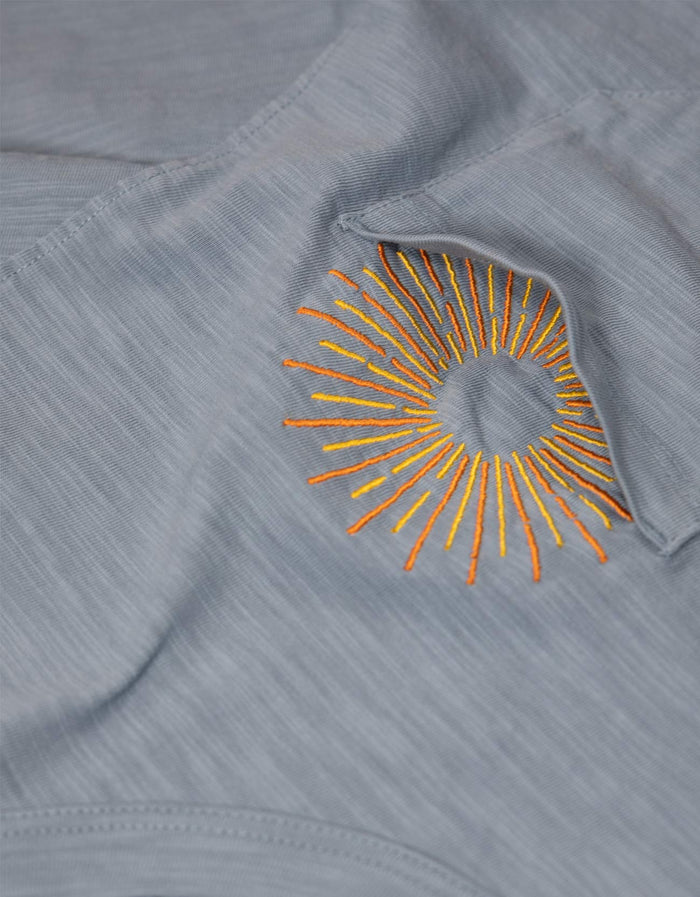 Close-up of the embroidered sun graphic on the chest pocket of the Baja Llama Sun Dreams Slub Pima Pocket Tee, showcasing the textured blue slub cotton fabric.