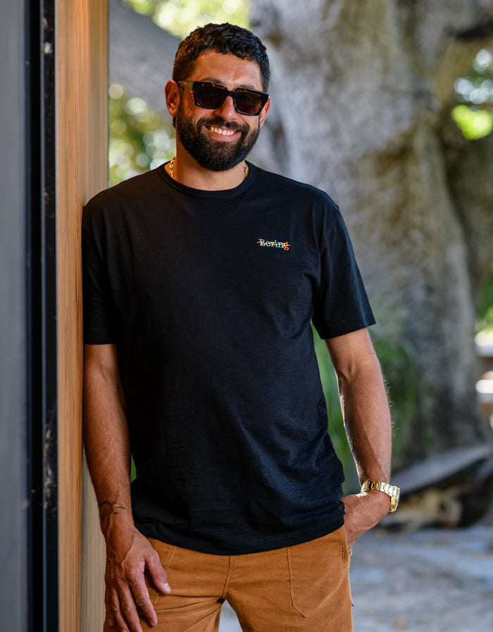 Man wearing a black slub pima cotton t-shirt with 'Boring' chest embroidery