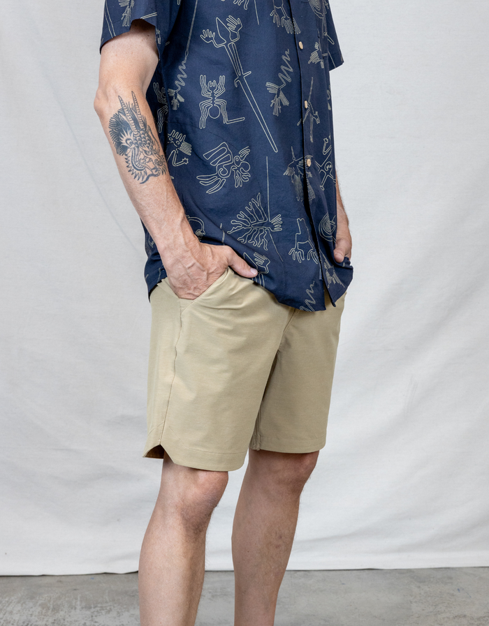 A man wearing Baja Llama Magellan Explorer shorts in Khaki Safari color with a dark blue patterned button-up shirt against a neutral studio background.