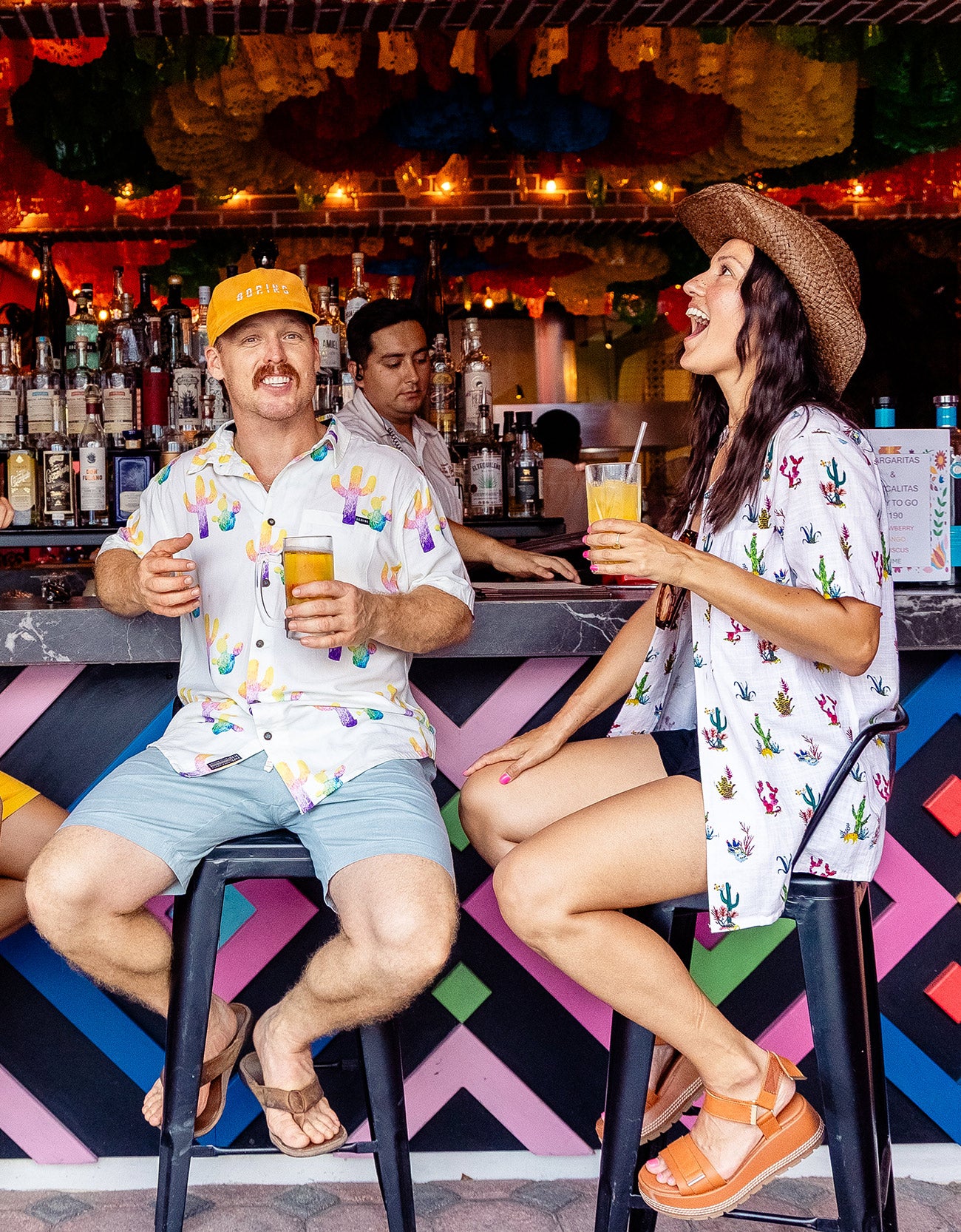 Man wearing the Baja Llama Colorful Cactus Cream Nighthawk™ Relaxed Fit Button Up shirt sitting at a bar with a friend