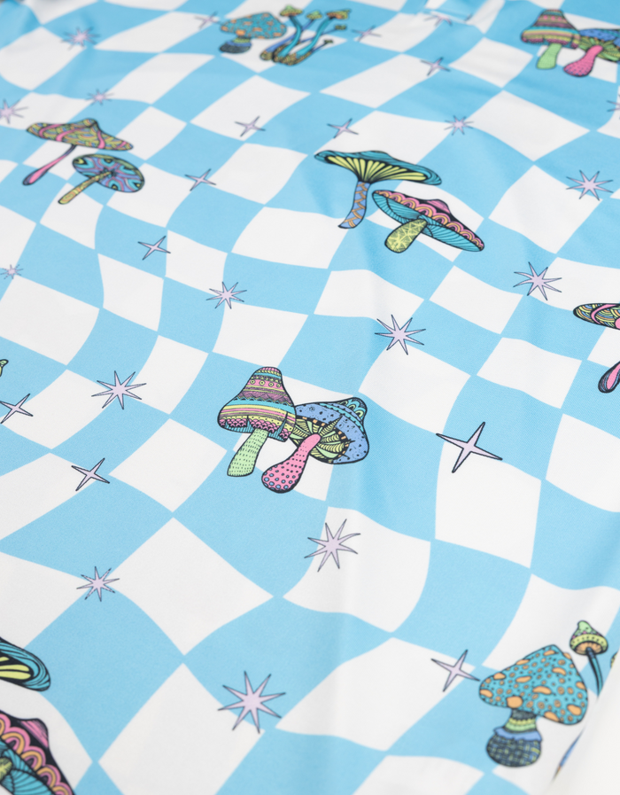 Close-up fabric detail of the Baja Llama Trip of a Lifetime Swingers Performance Polo, featuring a vibrant blue checkerboard pattern with colorful mushroom and star accents.