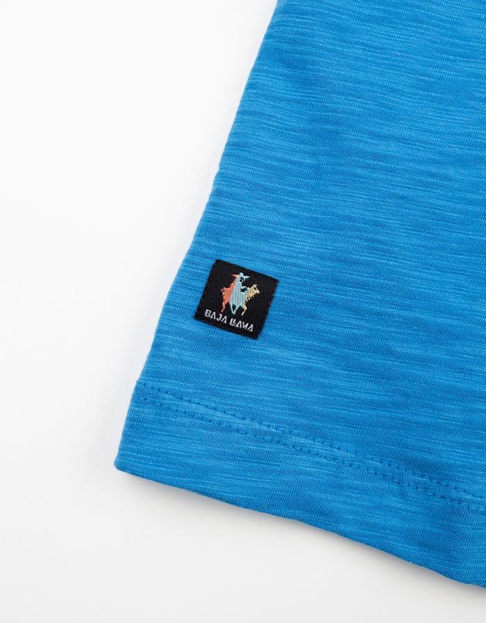 Close-up detail of the Baja Llama logo tag on the blue slub pima pocket tee.