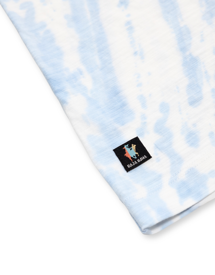 Close-up of the Baja Llama woven brand label on the hem of the Trip of a Lifetime Slub Pima Pocket Tee, featuring blue tie-dye fabric texture.
