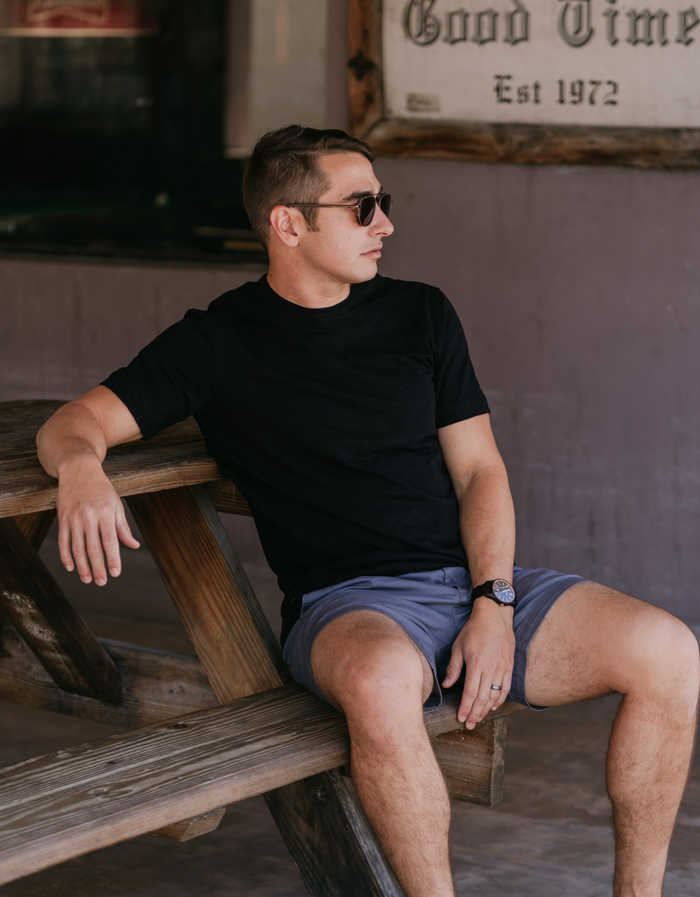 Man on picnic bench wearing black Solid Slub Pima tee with slate shorts and sunglasses