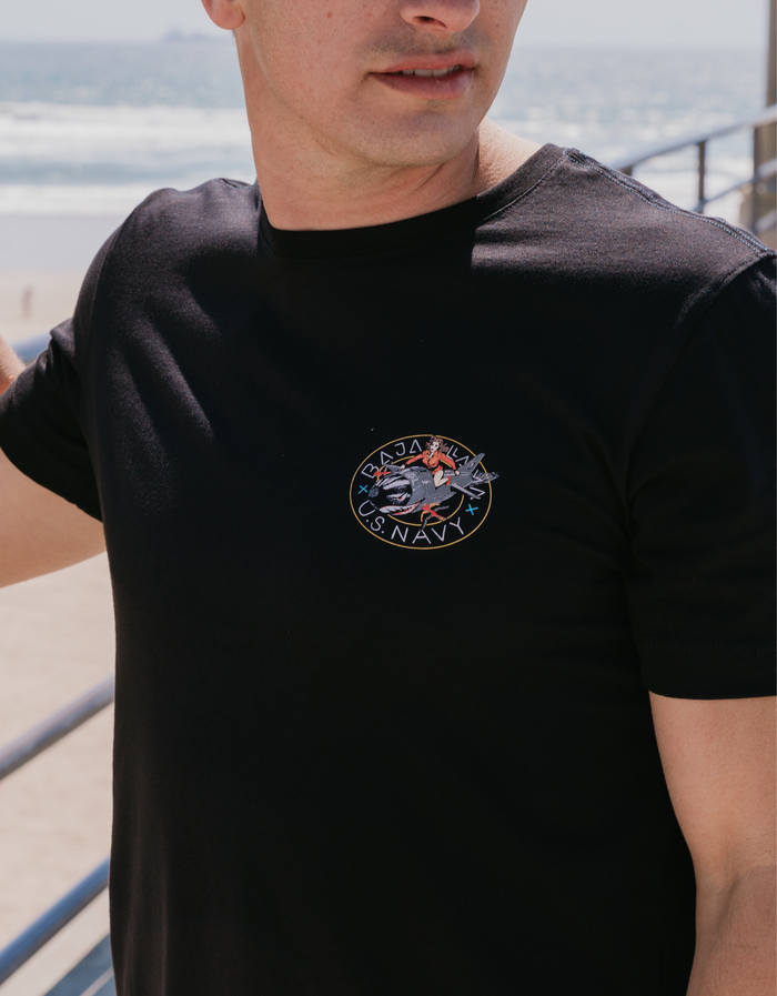 Man wearing the Baja Llama Sailor Stories Octopus black Primo graphic tee, featuring a detailed chest logo design while standing at the beach.