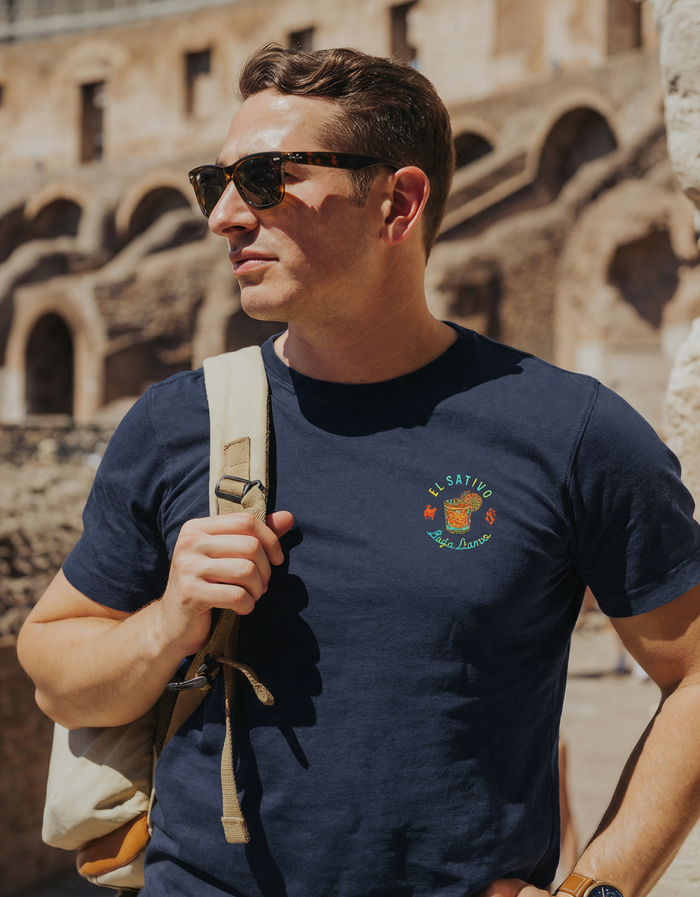 Lifestyle torso view of navy El Sativo Primo tee with cocktail chest graphic near stone arches