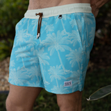 green swim shorts with palm tree pattern worn by a person outdoors.