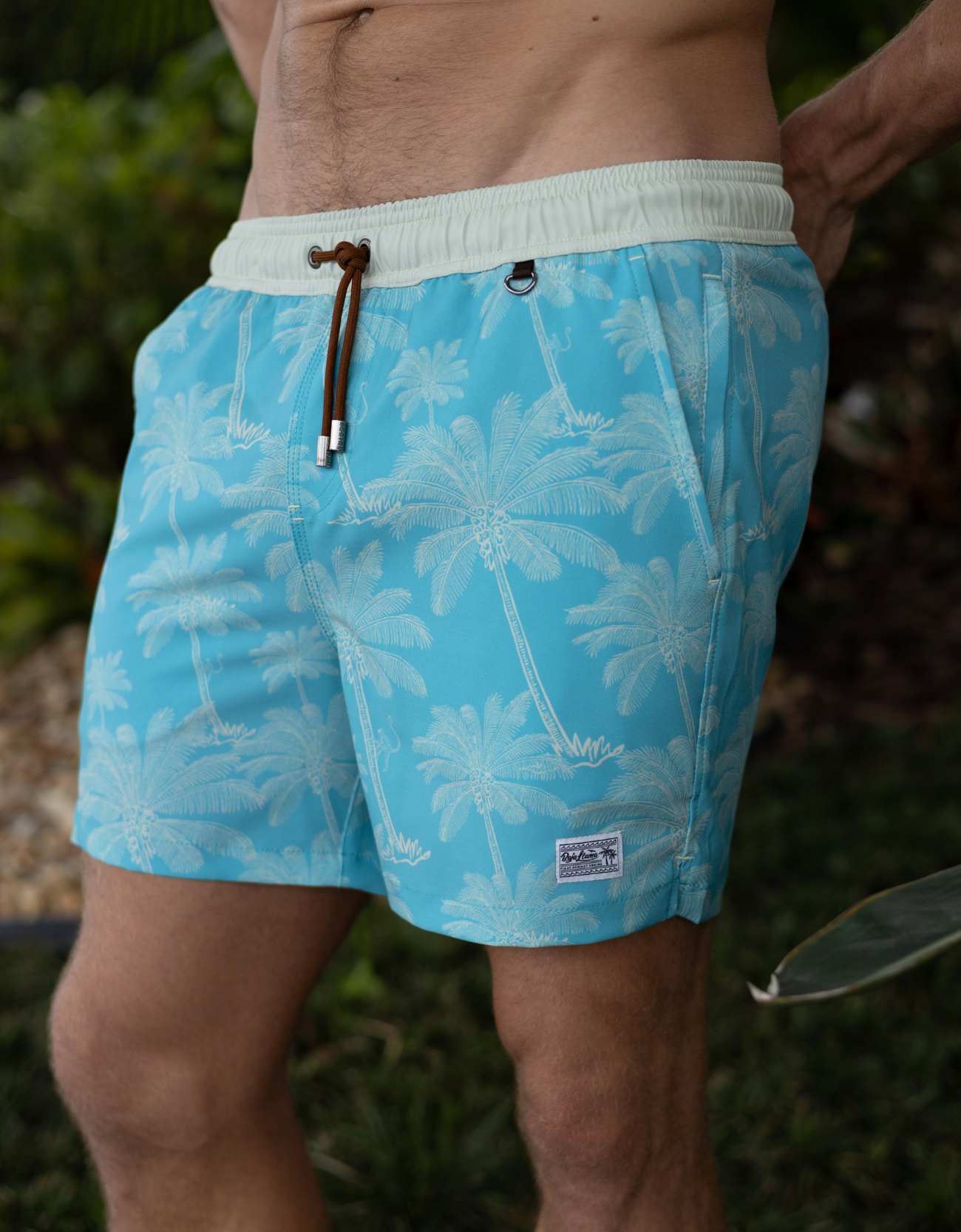green swim shorts with palm tree pattern worn by a person outdoors.