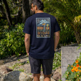 Rear view of a man walking outdoors showcasing the large Electric Palm graphic on the back of his navy blue Baja Llama Primo Graphic Tee