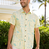 Man wearing a music patterned yellow shirt standing outdoors with greenery and a gazebo in the background