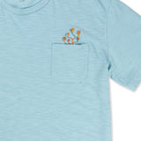 A close-up shot of the neckline and chest area on the Baja Llama El Sativo Cacti Pima Slub Pocket Tee, showing the porcelain blue textured fabric, a patch pocket with an embroidered orange and green cactus