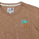 A close-up shot of the neckline and chest area on the Baja Llama La Republica Embroidered Pima Slub Pocket Tee, showing the brown textured fabric, a stitched pocket with an embroidered teal banana tree, and a geometric pattern on the inner collar.