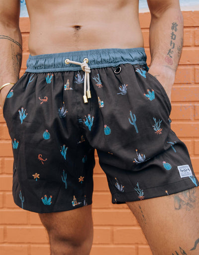 Black men's swim trunks featuring different cactus prints in blue and orange highlights.