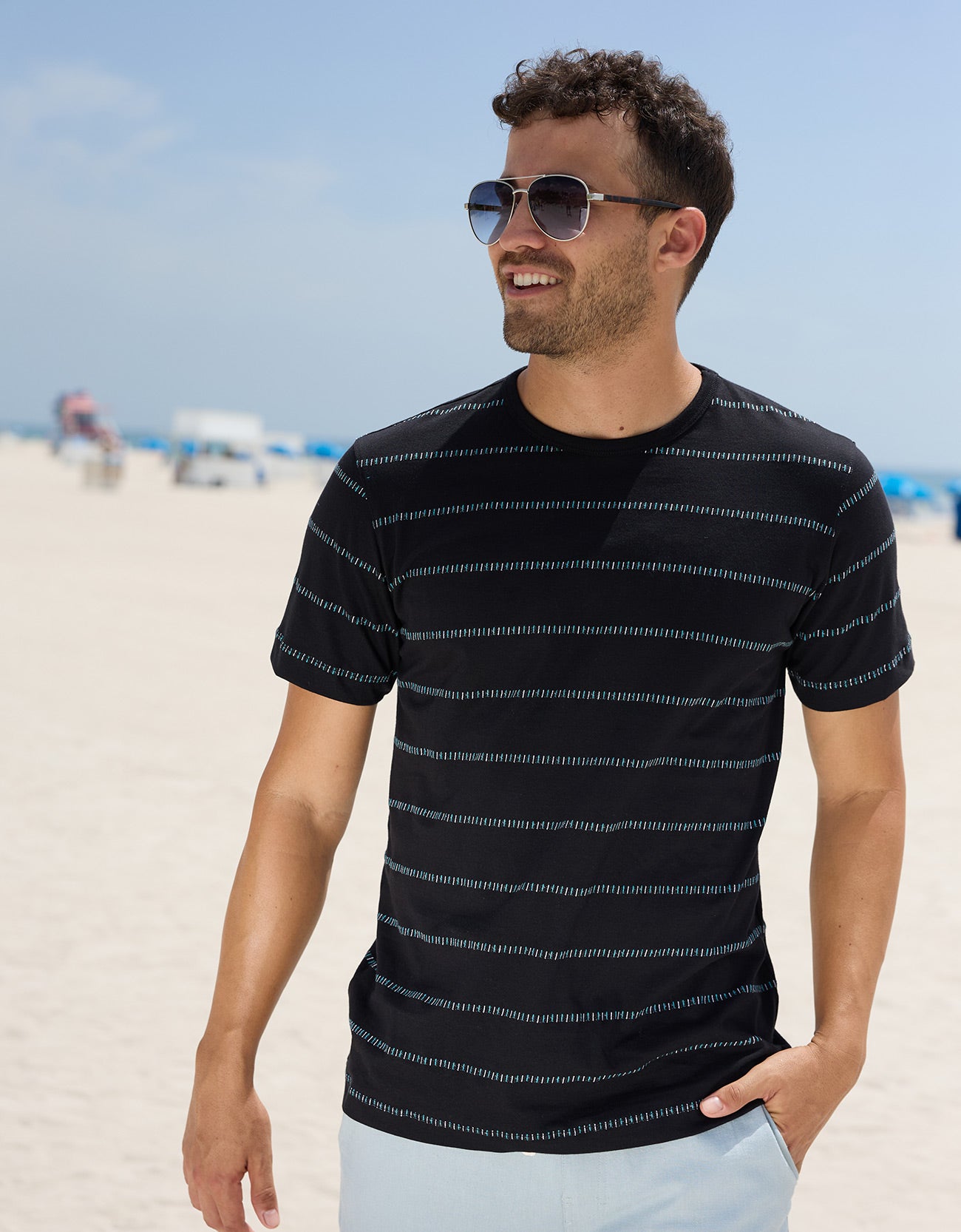 Lifestyle photo of a man wearing a black striped jacquard short-sleeve t-shirt outdoors near the ocean