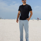 Full-length view of a man wearing the Black Onassis Jacquard Tee by Baja Llama at the beach