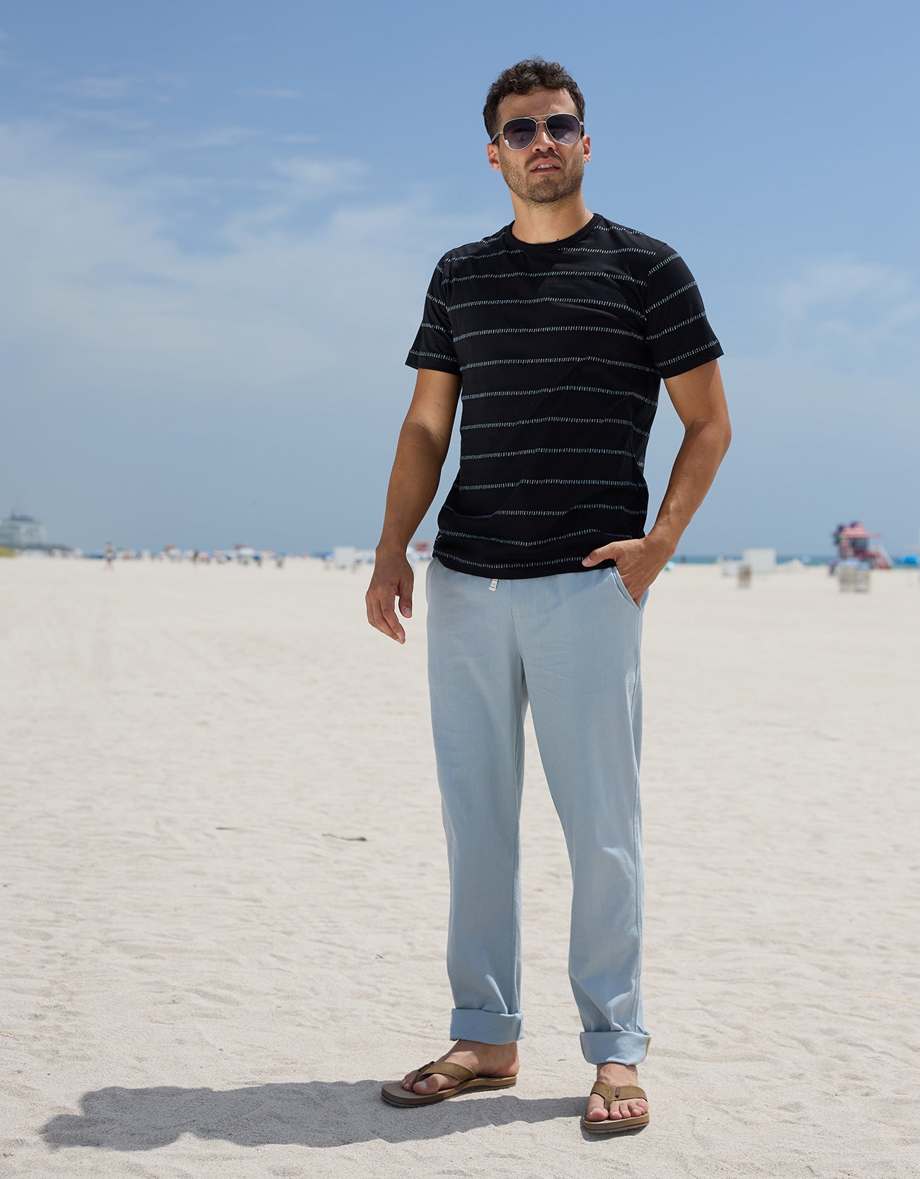 Full-length view of a man wearing the Black Onassis Jacquard Tee by Baja Llama at the beach