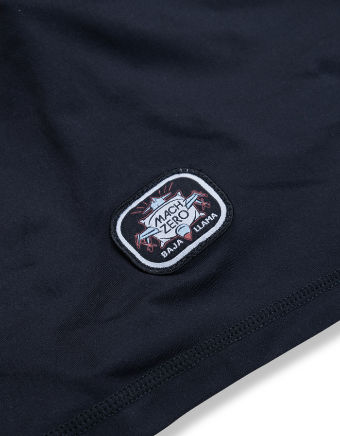 Close-up of the Baja Llama Mach Zero branding patch on the retro black lounge shorts.