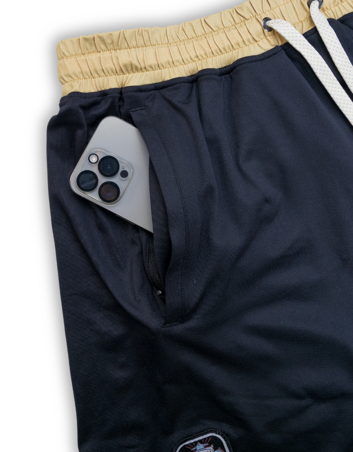 Close-up of the Baja Llama Mach Zero lounge shorts in retro black, highlighting the functional zippered pocket with a smartphone inside.
