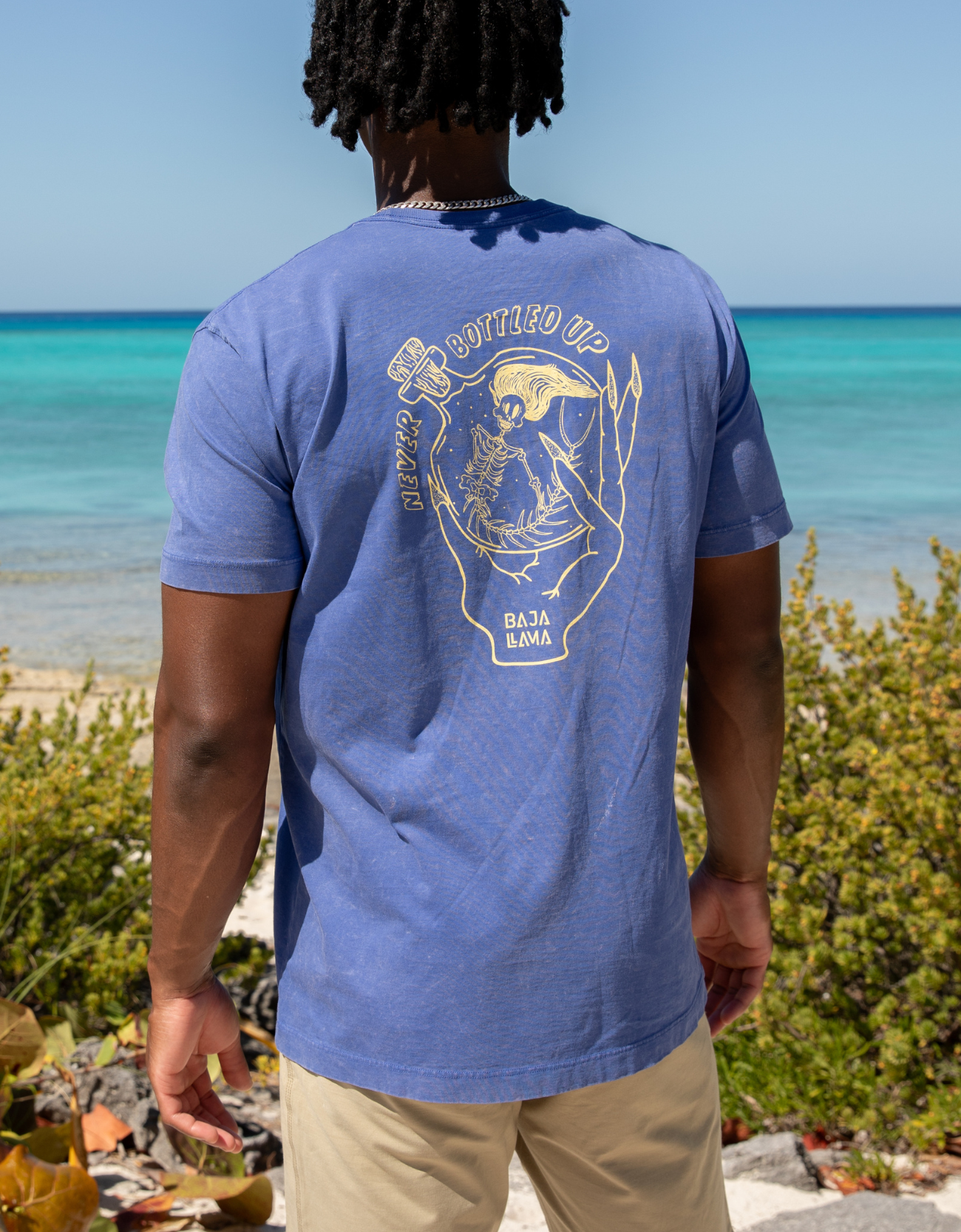 Never Bottled Up graphic tee by Baja Llama. Blue tee featuring a light yellow hand drawn skeleton mermaid. Soft fabric and relaxed fit for adventurous style.