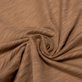 Detailed close-up of a soft, scorched brown slub-knit cotton fabric arranged in a spiral, showing the fine texture and weave.