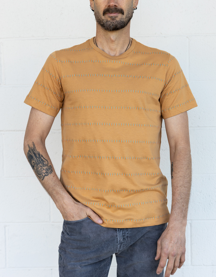 Man wearing a mustard yellow/camel striped t-shirt against a white wall