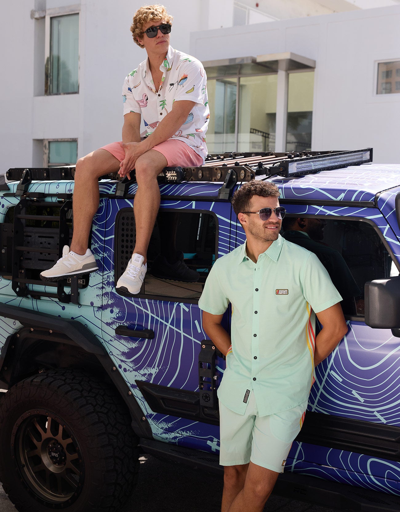 Man leaning against a vehicle wearing the Baja Llama Go Fast Green Vagabond Button Up shirt and matching shorts