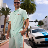 Man wearing Baja Llama Go Fast Green Vagabond Button Up shirt and matching shorts outdoors with a sports car
