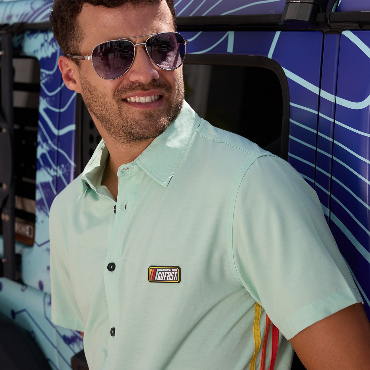 Baja Llama Go Fast Green Vagabond Button Up shirt worn by a man wearing sunglasses next to a vehicle