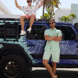 Two men posing outdoors by a vehicle with one wearing the Green Vagabond Go Fast button up set