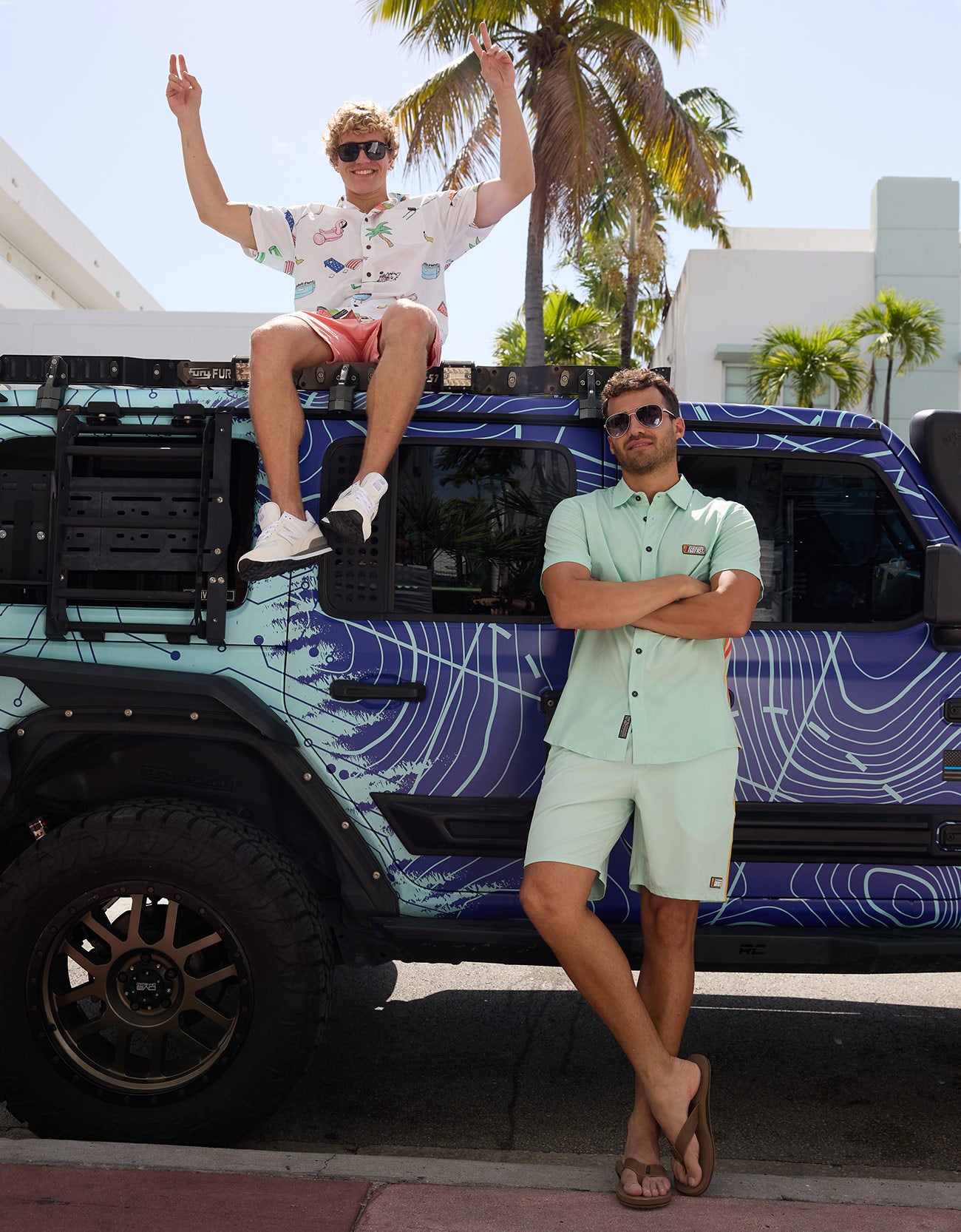 Two men posing outdoors by a vehicle with one wearing the Green Vagabond Go Fast button up set