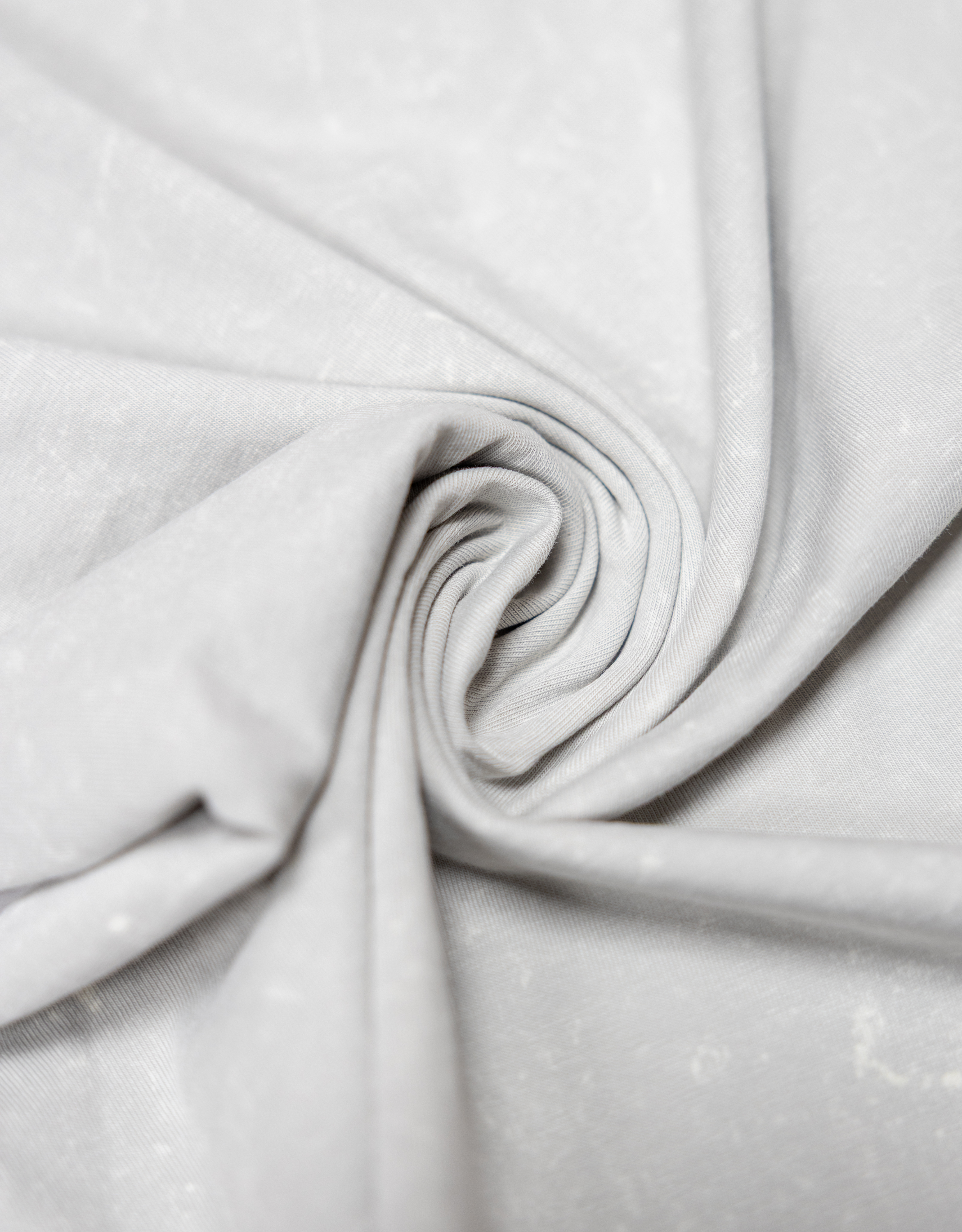 Detailed shot of the Baja Llama Greatful Dyed Shoreline Smoke Heavy Tee fabric, tightly swirled to showcase its heavy cotton texture and vintage-wash light gray color.