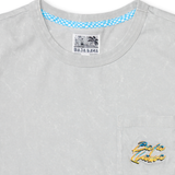 Close-up of the collar and upper chest area of the Baja Llama Greatful Dyed Shoreline Smoke Heavy Tee, showing the crew neck, blue checkered inner neck tape, and a chest pocket with a yellow and blue embroidered cursive brand logo