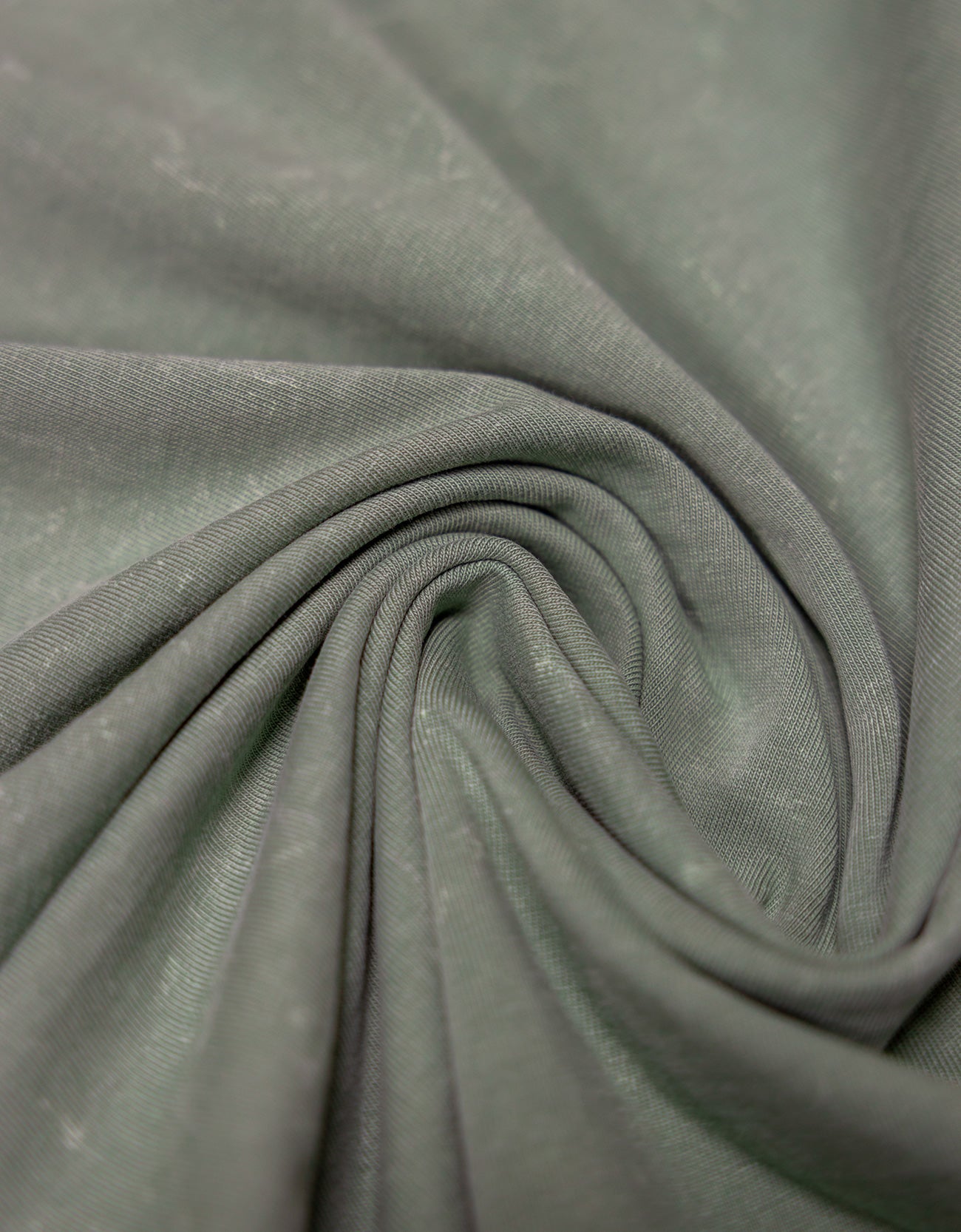 A close-up view of the Baja Llama Greatful Dyed Rock On Cypress Green Heavy Tee fabric, tightly swirled to display the heavy cotton texture and vintage-wash olive green color.