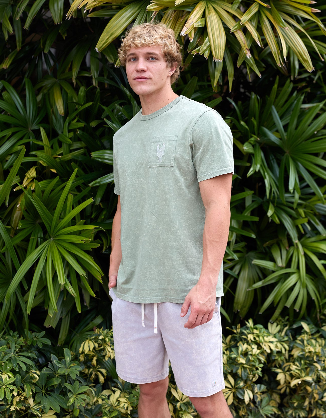 Man wearing the Baja Llama Greatful Dyed - Rock On Cypress Green Heavy Tee outdoors among tropical foliage