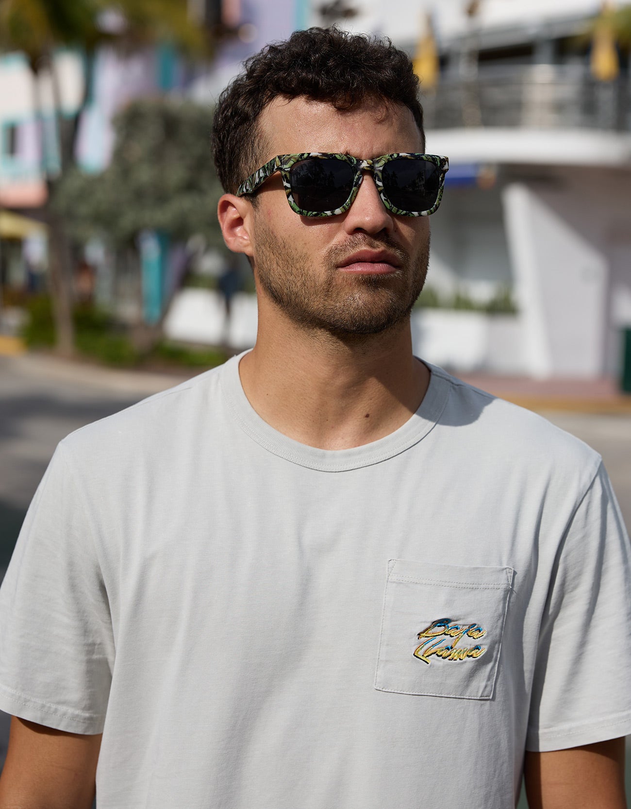 Model wearing the Greatful Dyed Shoreline Smoke Heavy Tee by Baja Llama with close-up of pocket logo and sunglasses