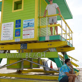 Man standing on a Miami Beach lifeguard tower wearing the Baja Llama Greatful Dyed - Shoreline Smoke Heavy Tee