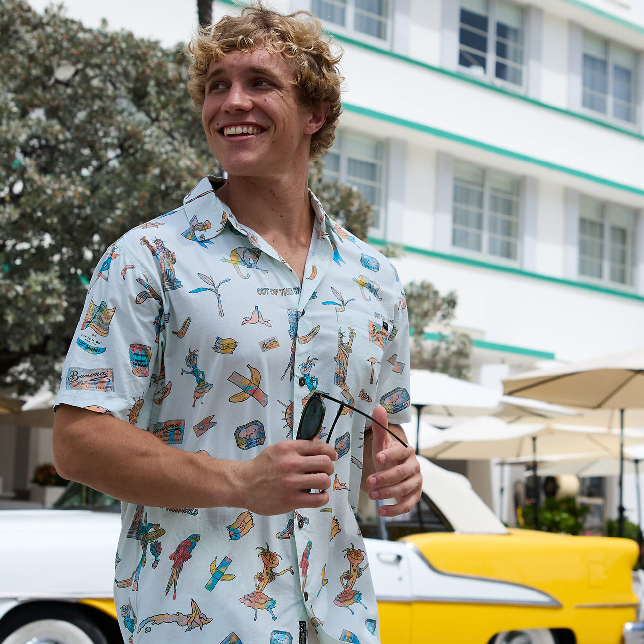 Model wearing the La Republica Bananera Icy Mint 7-Seas Relaxed Fit Button Up shirt by Baja Llama outdoors with vintage car