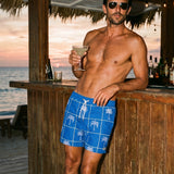 Man in blue swim shorts holding a cocktail at a beach bar